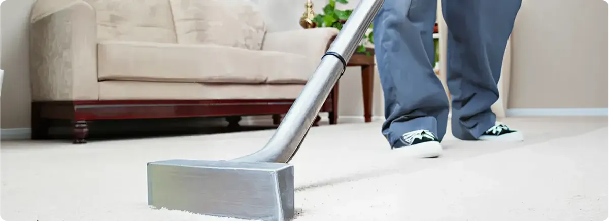Carpet cleaning technician using a hot-water extraction wand on a light-colored carpet in a living room, Anchorage, AK.